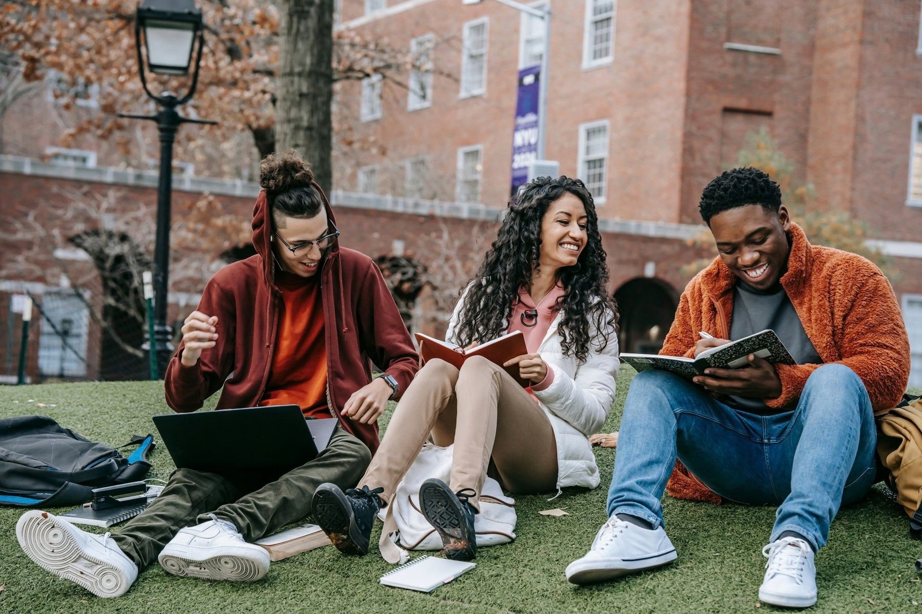 Three students laughing and studying together on a campus lawn